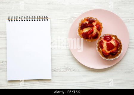 Fromage à la crème aux fraises tartelettes sur la plaque rose avec un ordinateur portable, vue du dessus. À partir de ci-dessus, les frais généraux. Banque D'Images