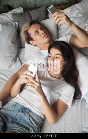 Millénaire toxicomanes couple relaxing in bed using smartphones Banque D'Images