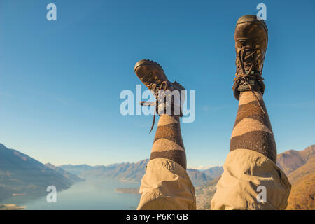 Des chaussures de randonnée et les jambes en l'air sur la chaîne de montagnes des Alpes et du Lac Majeur au Tessin, Suisse. Banque D'Images