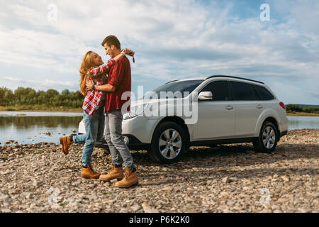 Jeune couple, habillé en blanc T-shirt et chemise à carreaux hugging près de la voiture et les rivières Banque D'Images