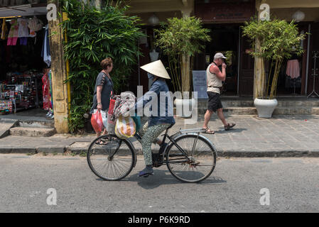 Hoi An, Vietnam--Mars 23, 2016. Une femme rides son vélo passé stocke dans une rue commerçante animée à Hoi An au Vietnam. Banque D'Images