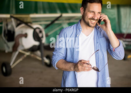 Beau jeune homme à l'aide de téléphone mobile dans le hangar avion Banque D'Images