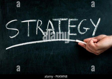 La main avec craie blanche soulignant la stratégie manuscrites texte sur tableau noir Banque D'Images