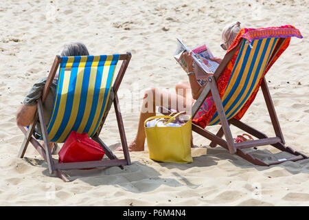 Bournemouth, Dorset, UK. 1er juillet 2018. Météo France : hazy sunshine, mais encore chaud comme des milliers d'sunseekers tête à la plages de Bournemouth à profiter d'une journée à la mer. Couple de chaises longues sur la plage, la lecture de journal. Credit : Carolyn Jenkins/Alamy Live News Banque D'Images