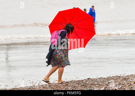 La ville de Sidmouth, Devon, UK. 1er juillet 2018. Météo britannique. Une femme sur la plage à la station balnéaire de Sidmouth dans le Devon avec parapluie comme la ville attrape le bord d'une adoption forte pluie douche. Crédit photo : Graham Hunt/Alamy Live News Banque D'Images
