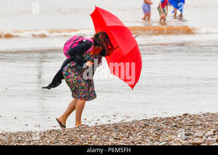 La ville de Sidmouth, Devon, UK. 1er juillet 2018. Météo britannique. Une femme sur la plage à la station balnéaire de Sidmouth dans le Devon avec parapluie comme la ville attrape le bord d'une adoption forte pluie douche. Crédit photo : Graham Hunt/Alamy Live News Banque D'Images