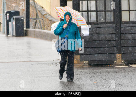 La ville de Sidmouth, Devon, UK. 1er juillet 2018. Météo britannique. Une femme sur le front de mer de la station balnéaire de Sidmouth dans le Devon avec parapluie comme la ville attrape le bord d'une adoption forte pluie douche. Crédit photo : Graham Hunt/Alamy Live News Banque D'Images
