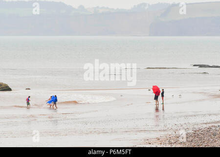 La ville de Sidmouth, Devon, UK. 1er juillet 2018. Météo britannique. Les visiteurs sur la plage à la station balnéaire de Sidmouth dans le Devon avec un parapluie comme la ville attrape le bord d'une adoption forte pluie douche. Crédit photo : Graham Hunt/Alamy Live News Banque D'Images
