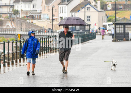 La ville de Sidmouth, Devon, UK. 1er juillet 2018. Météo britannique. Les promeneurs de chiens sur le front de mer de la station balnéaire de Sidmouth dans le Devon avec un parapluie comme la ville attrape le bord d'une adoption forte pluie douche. Crédit photo : Graham Hunt/Alamy Live News Banque D'Images