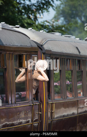 Kidderminster, Royaume-Uni. 1er juillet 2018. Le voyage nostalgique de retour dans le temps se poursuit à Severn Valley Railway alors que nous tournons l'horloge vers les années 1940. Une dame en robe polkadot d'époque (vue de derrière) tient sur son chapeau de paille, se penche hors de la fenêtre de la voiture de chemin de fer alors que le train à vapeur en mouvement commence son départ de la gare d'Arley. Crédit : Lee Hudson/Alay Live News Banque D'Images