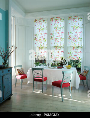 Aveugles floral sur une grande fenêtre dans la salle à manger avec parquet en bois et des chaises rouges assis à table avec un chiffon blanc Banque D'Images