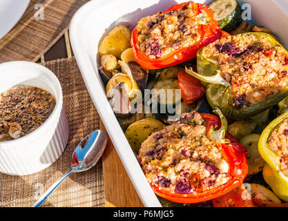 Poivrons rôtis farcis dans un plat en céramique sur un lit de légumes rôtis et de pommes de terre avec une vinaigrette au yaourt épicé sur une table extérieure au soleil Banque D'Images
