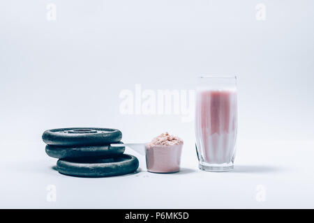 Whey Protein Shake dans verre à côté d'écope de poudre sèche et pile de disques d'haltère sur fond blanc. Les suppléments de nutrition pour boire et lourd Banque D'Images