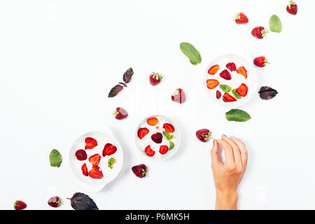 Woman's hand prendre des fraises fraîches entre les bols de glace sur fond blanc, vue du dessus. Arrangement de l'été mise à plat desserts froid décoré wi Banque D'Images