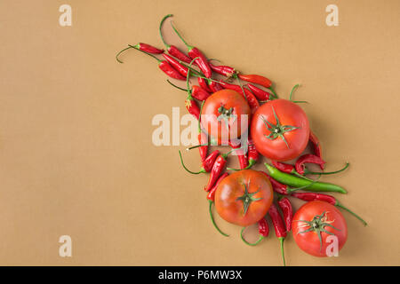 Bio frais mûrs tomates rouges Hot Chili Peppers organisé sur fond brun. Espagnol Grec Italien mexicain Cuisine Méditerranéenne. Le régime alimentaire sain Banque D'Images