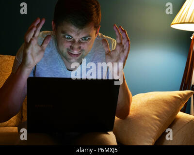 Homme en colère la lecture des informations à l'ordinateur portable dans la chambre. Banque D'Images