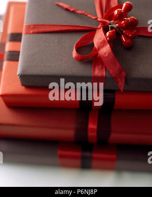 Close-up d'une pile de cadeaux de Noël cadeau enveloppé de papier rouge et gris foncé et attachés à un ruban de soie rouge Banque D'Images