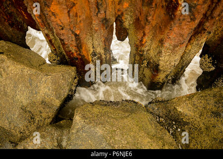 De grands rochers et de métal rouillé dans l'eau par plage de sable et des eaux agitées Banque D'Images