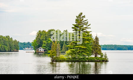 Petite île dans le lac Muskoka avec un chalet et bateau d'excursion dans l'arrière-plan. Banque D'Images