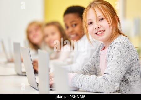 Girl est l'apprentissage en classe primaire classe d'ordinateur portable avec des amis à Banque D'Images