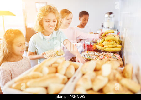 Des enfants heureux d'apporter de la nourriture au buffet d'une cantine à l'école Banque D'Images