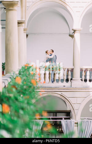 Beau palefrenier est d'embrasser le smiling bride dans la joue sur le beau balcon plein de fleurs. Banque D'Images