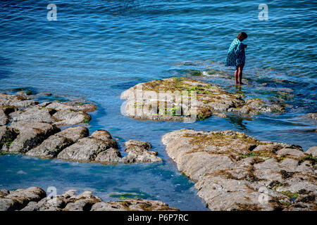 Une femme jouit de la météo sur des rochers sur le rivage à Combe Martin sur la côte nord du Devon à mesure que la température continue de monter l'ensemble du Royaume-Uni. Banque D'Images