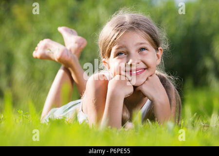 Heureux sourire petite fille à l'école élémentaire âge allongé sur l'herbe verte dans le parc Banque D'Images
