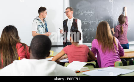 Personnes âgées teacher standing près du tableau noir et demandant aux élèves à la leçon de mathématiques Banque D'Images