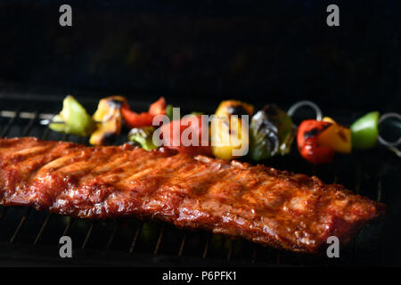 Carré de côtes levées barbecue cuisson sur un barbecue avec des poivrons verts et rouges, fond sombre pour copy space Banque D'Images