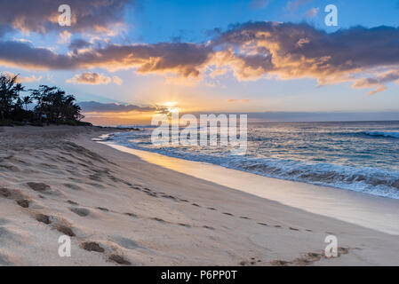 Coucher de soleil sur Sunset Beach sur la côte nord d'Oahu, Hawaï avec surf s'abattant sur les rochers sur la plage de sable Banque D'Images