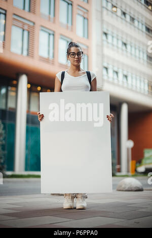 Belle jeune femme à lunettes holding blank canvas sur la rue. Banque D'Images
