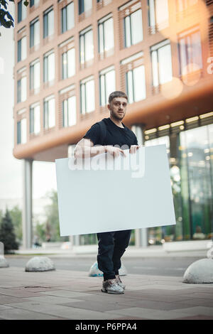 Jeune homme tenant toile vierge horizontalement et en regardant le spectateur. Banque D'Images