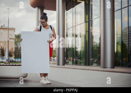 Young attractive woman holding blank canvas et regarder dans la rue. Banque D'Images