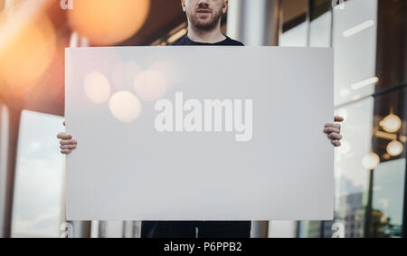 Close up of attractive man holding blank canvas sur l'horizontale de la rue. Banque D'Images