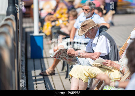 Skegness, UK. 2e juillet 2018. Comme les températures continuent à augmenter à travers le Royaume-Uni au cours de la vague de chaleur actuelle, un vieil homme est assis dans sa dekchair sur jetée de Skegness et lit son journal dans la lumière du soleil chaude. Crédit : Steven Booth/Alamy Live News. Banque D'Images