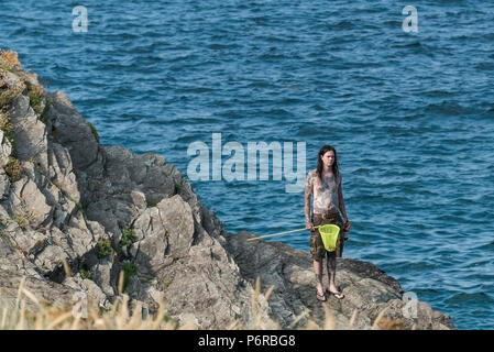 Un homme tatoué sur les rochers et debout tenant un filet de pêche et une bouteille. Banque D'Images