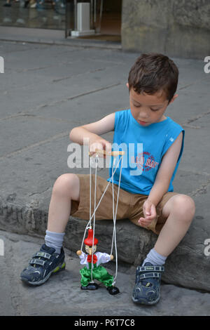 Un jeune garçon assis sur le trottoir à Florence, en Italie, joue avec une marionnette de Pinocchio Banque D'Images