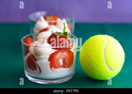 Wimbledon inspiré de la crème fouettée, des meringues et de fraises fraîches dans un bol en verre sur un fond violet et vert avec une balle de tennis Banque D'Images