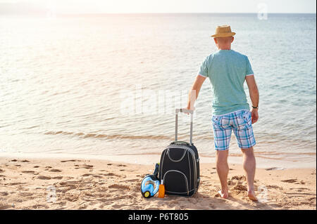 L'homme dans des vêtements d'été avec une valise à la main, regardant la mer sur la plage, notion de temps pour voyager Banque D'Images
