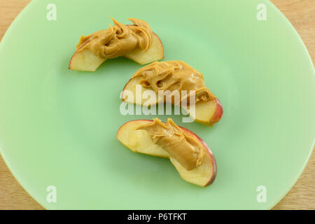 Close up de tranches de pomme avec du beurre d'arachide sur plaque verte Banque D'Images