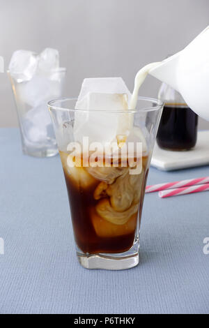 Le lait est versé dans un verre à eau froide préparer du café et des cubes de glace. Banque D'Images