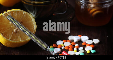 Médicaments et pilules sur une table en bois. Divers moyens pour prévenir les rhumes. Thé au citron et de miel. Tasse en verre avec plateau tranche de citron et un pot de miel. Banque D'Images