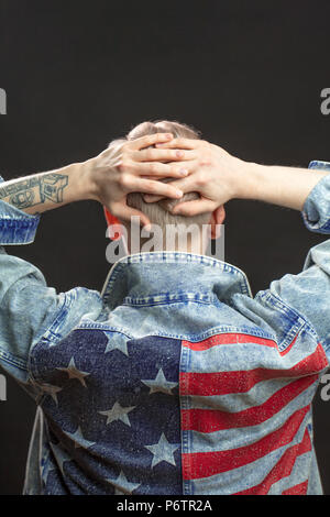 Vue arrière du mâle en denim jaket méconnaissable avec le drapeau américain et ont soulevé les bras tatoués jointes isolé sur fond noir la tête Banque D'Images