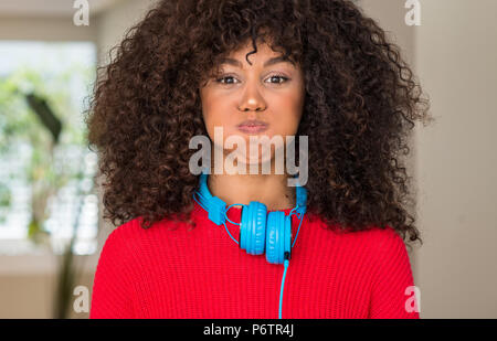 African American Woman wearing headphones puffing joues avec drôle de visage. Bouche gonflé à l'air, l'expression fou. Banque D'Images