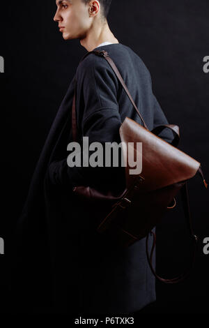 Les jeunes confiants s businessman looking at camera avec calme et grave expression habillé en manteau à la mode de porter à l'épaule Sac en cuir brun de l'autre côté Banque D'Images
