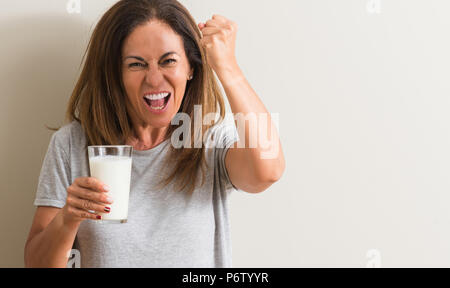 Moyen-âge femme à boire un verre de lait frais contrarié et frustré de crier avec colère, fou et hurlant de main levée, la colère concept Banque D'Images