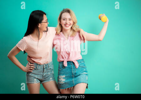 Portrait of young différentes nationalités teenage girlfriends, caucasiens et asiatiques - femme hagging, isolé sur fond bleu. European woman hold Banque D'Images