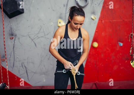 Athletic femme alpiniste dans le harnais de sécurité corde de liage en huit noeud et la préparation à l'ascension. Matériel d'escalade Banque D'Images