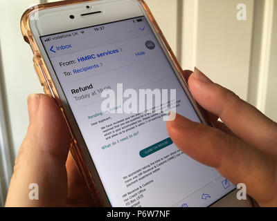 Téléphone mobile dans la main de femme avec un / des e-mails de phishing scam, prétendant provenir de l'HMRC, affichée sur l'écran Banque D'Images